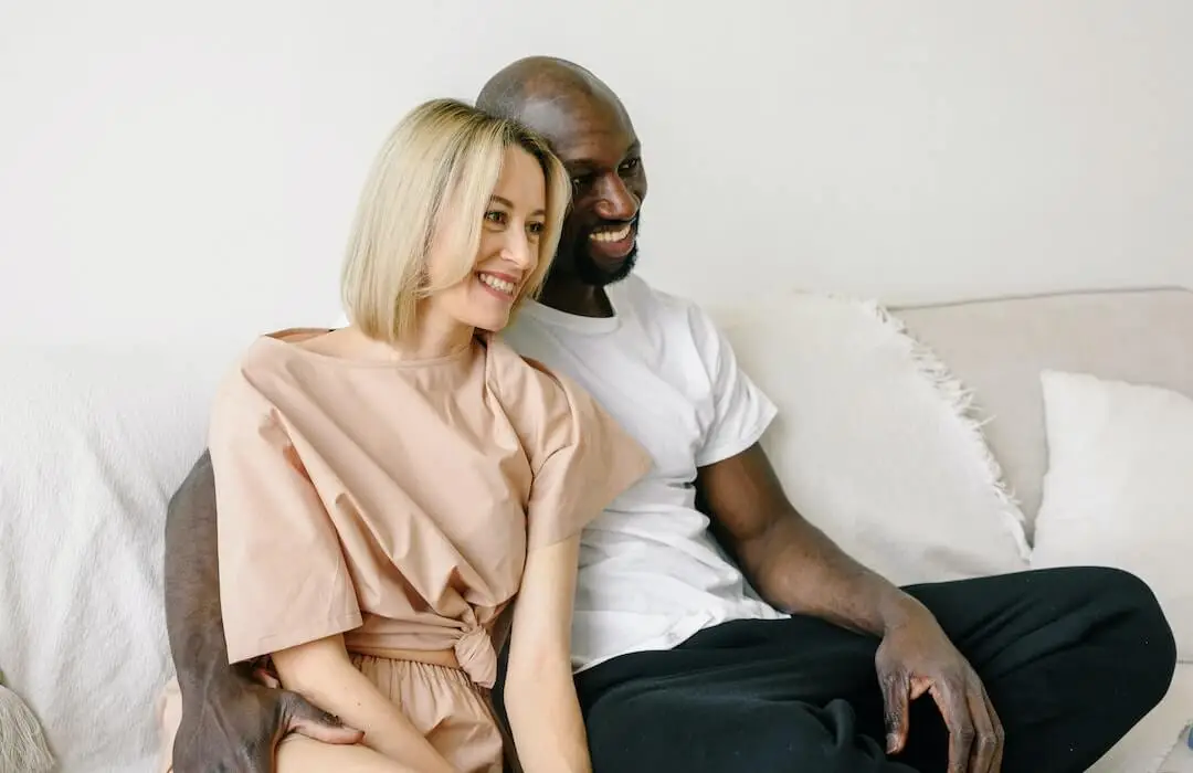 Black and White Couple Smiling while Sitting on Couch