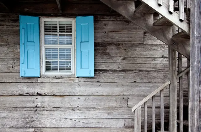 Weathered wood siding, blue shutters, and an exterior staircase