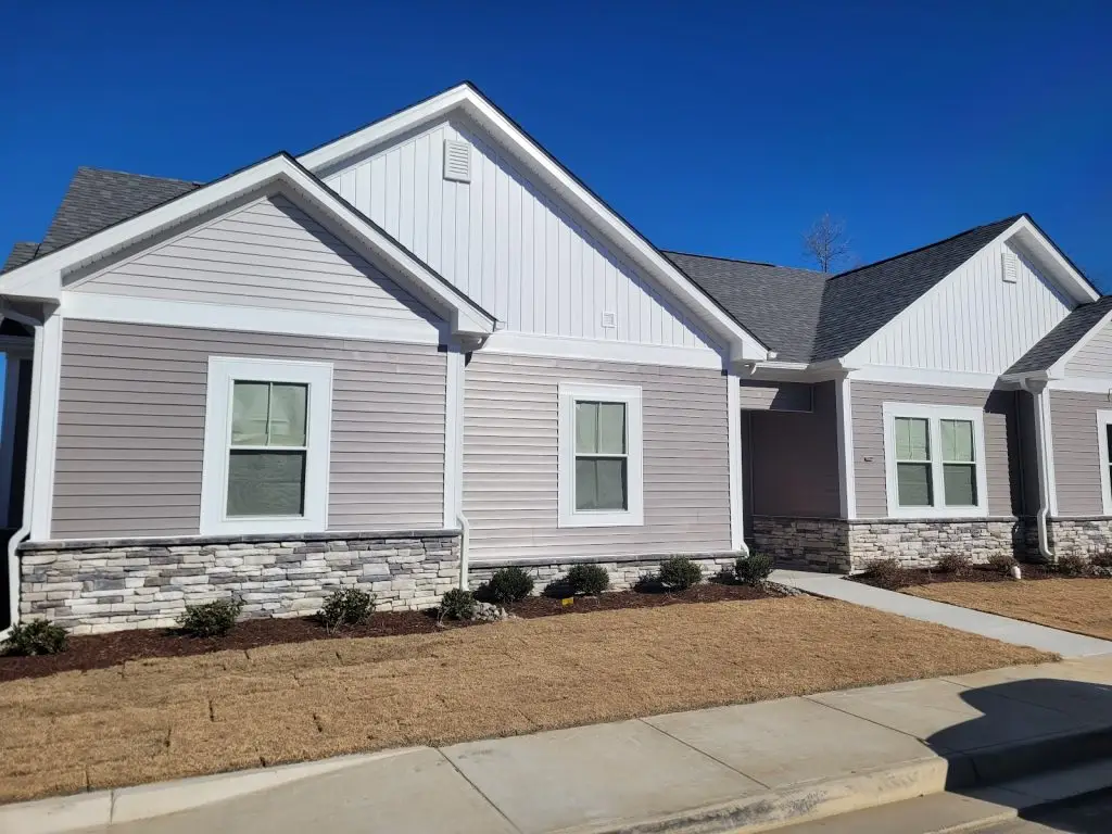 Gray home with white gables, stone accents, and a front walkway under a blue sky