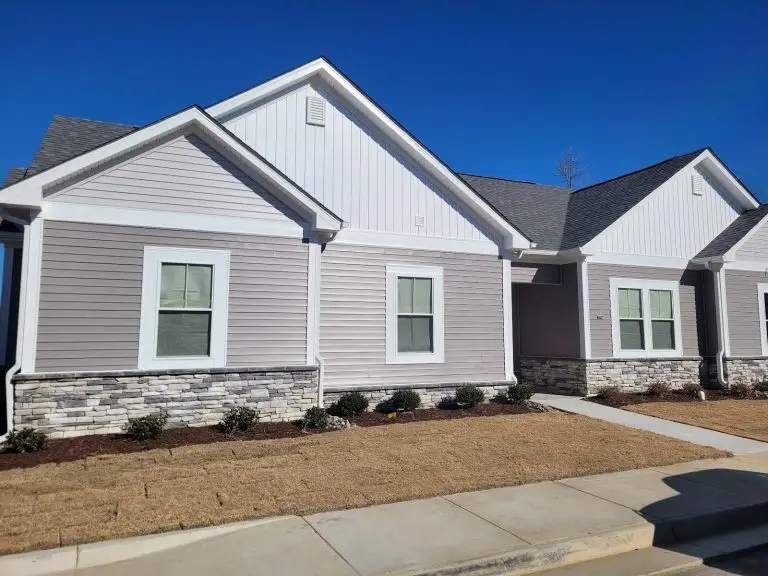 Gray home with white gables, stone accents, and a front walkway under a blue sky