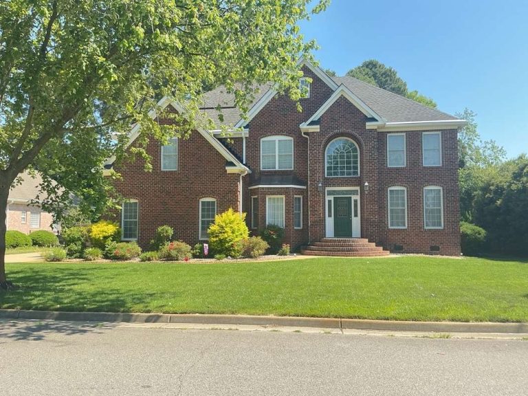 Front view of a two-story brick home with an arched entry window, landscaped shrubs, and a green lawn.