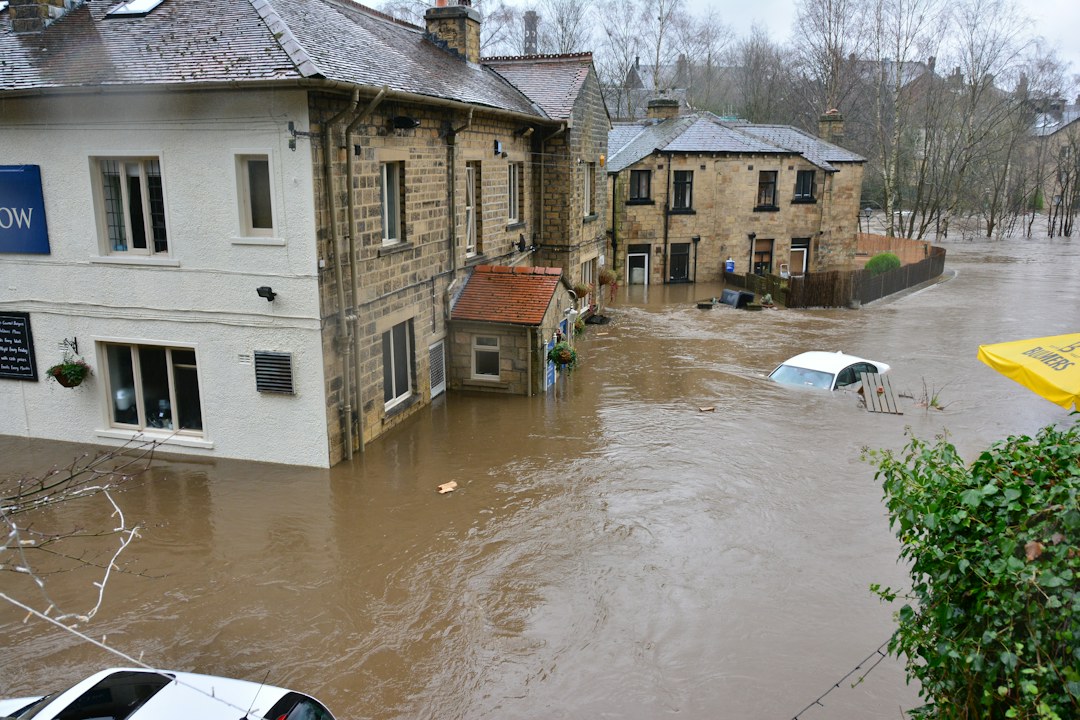 Floodwater surrounds stone buildings and a partially submerged white car in Bingley, England.