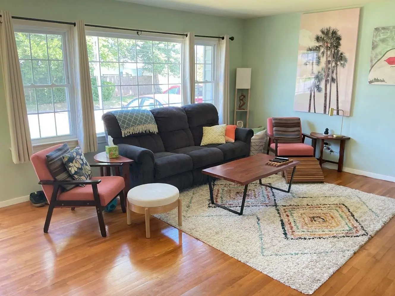 Living room with wood flooring, large windows, a sofa and two chairs