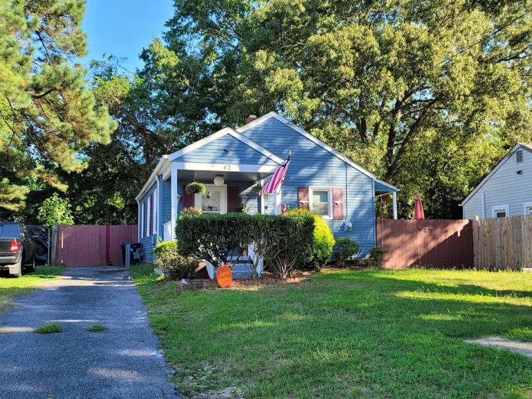 Blue bungalow with a front porch and green lawn beneath mature trees