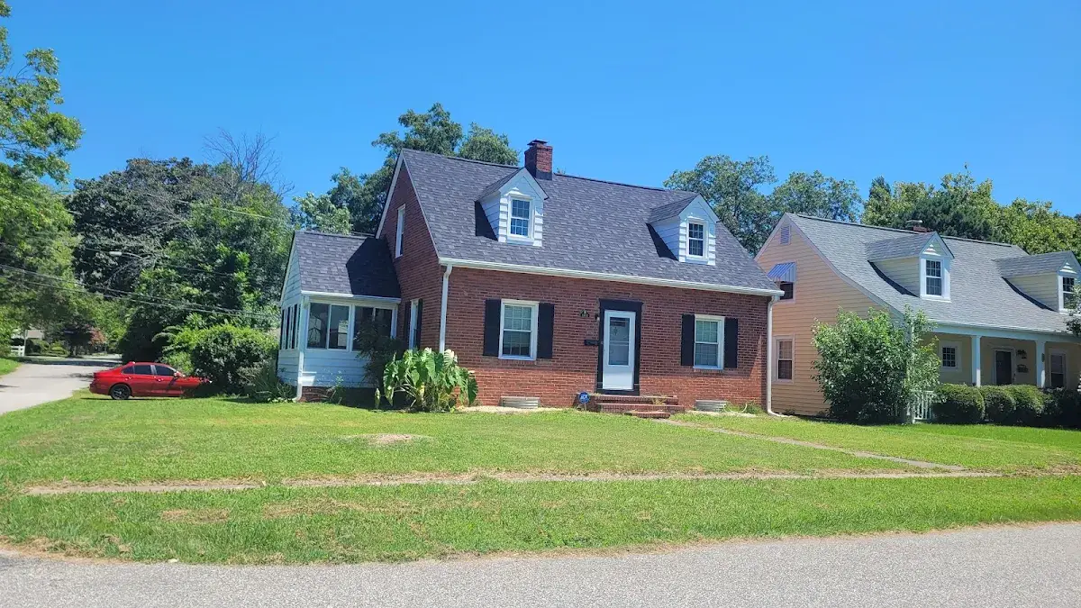 Brick Cape Cod home with a broad front lawn beneath a blue sky