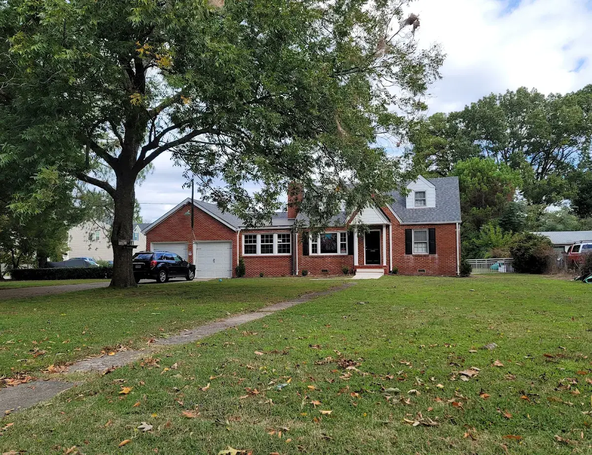 Brick Cape Cod home with a broad lawn and large mature tree