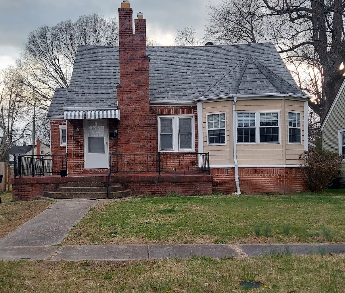 Brick Cape Cod home with a prominent chimney and front lawn