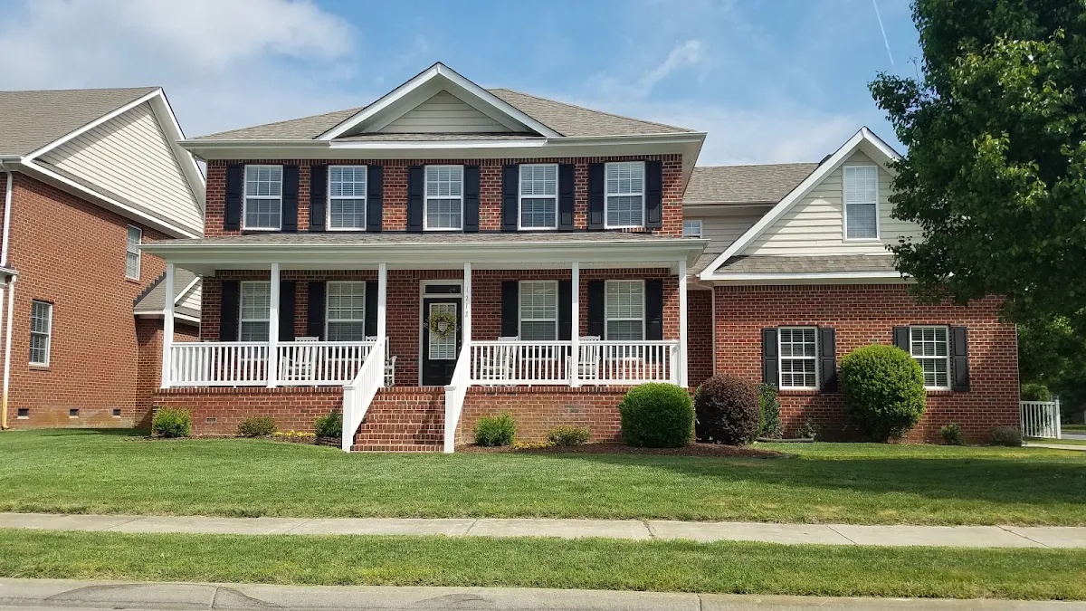 Brick two-story home with a wide white front porch, dark shutters and a green lawn
