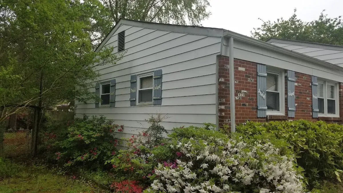 Brick and horizontal siding on a home beside shrubs and flowering azaleas.