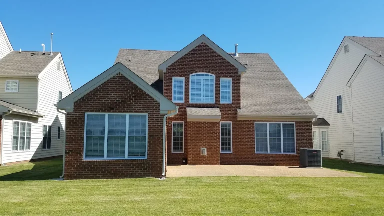 Rear elevation of a brick house with several gables and an open lawn