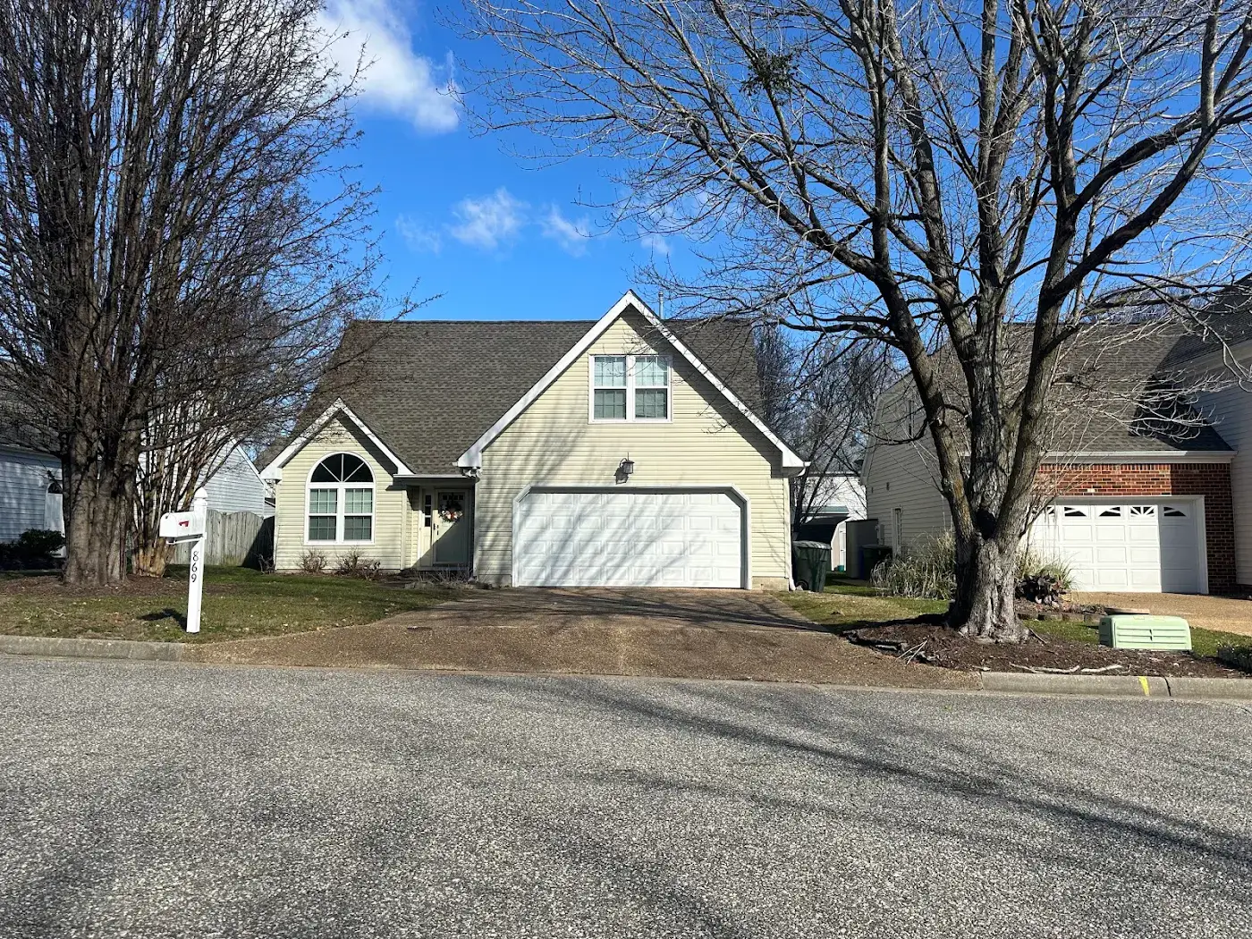 Light-colored gabled house with an attached garage and mature trees