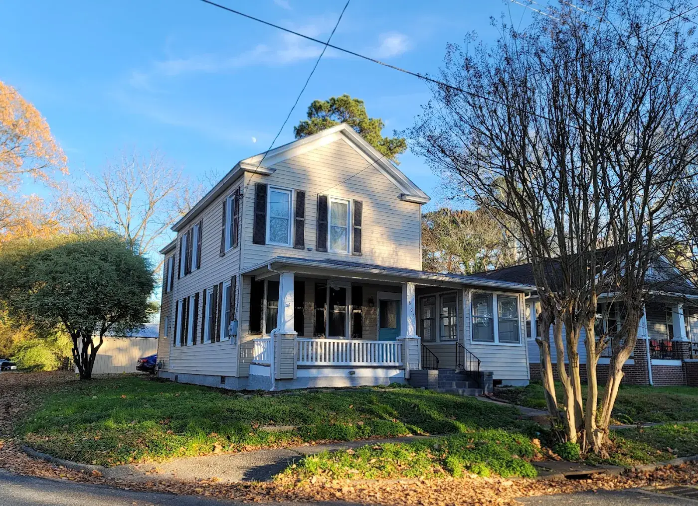 Two-story house with dark shutters, a wraparound porch and mature landscaping