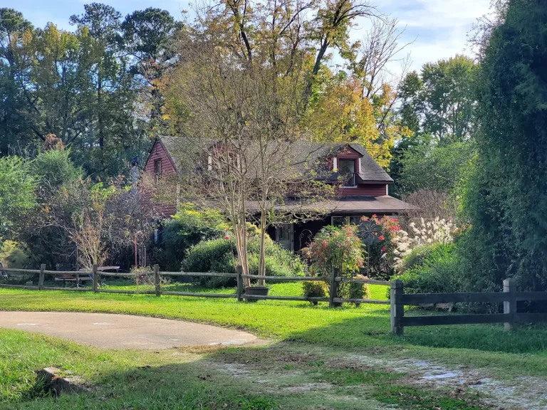 House with a covered porch, mature trees and a split-rail fence