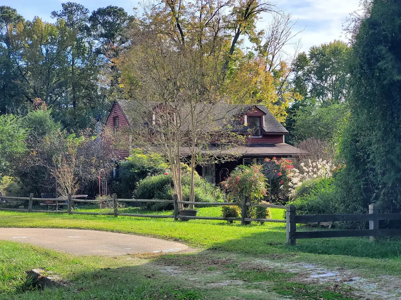 House with a covered porch, mature trees and a split-rail fence