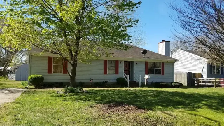 Pale green ranch home with orange shutters beneath mature trees