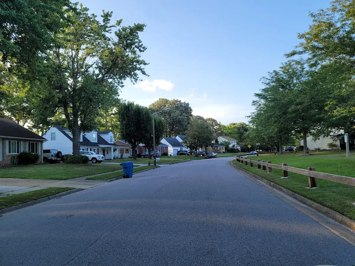 Residential street with green lawns, mature trees, and a white fence
