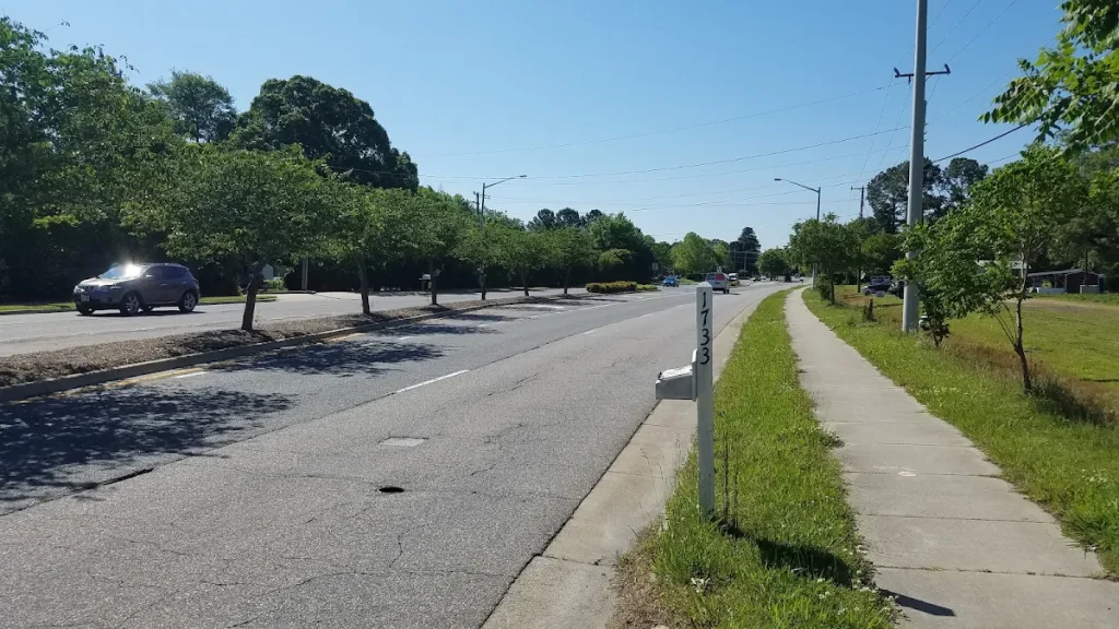 Road beside a sidewalk, open lawn, and overhead utility lines