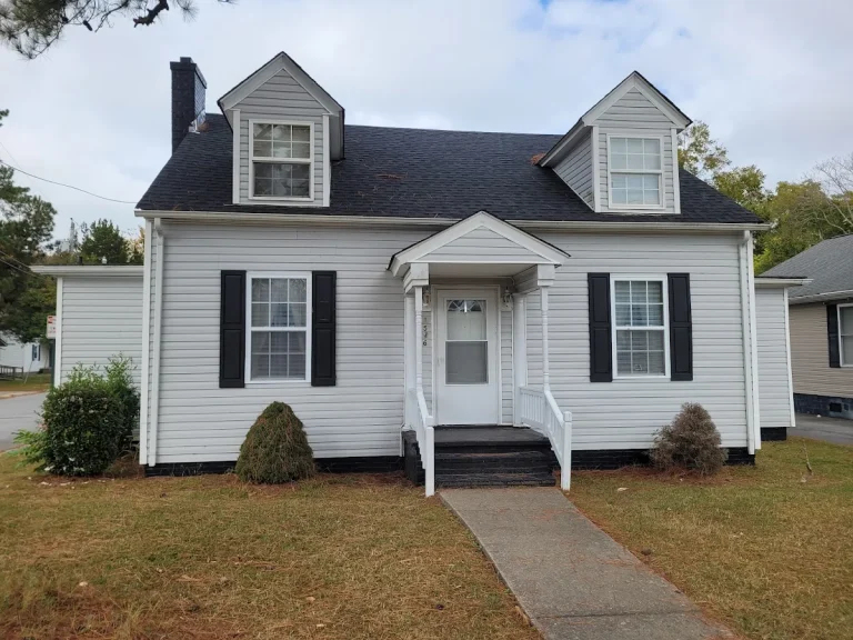 White Cape Cod home with two dormers, black shutters, and a front lawn