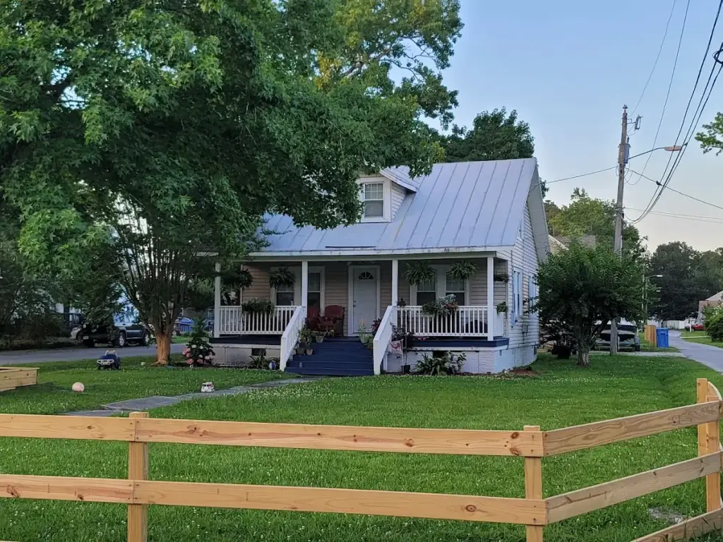 White cottage with a covered porch, metal roof, and wooden fence