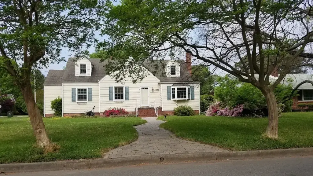 White home with dormers and a curved front walkway framed by trees and flowers