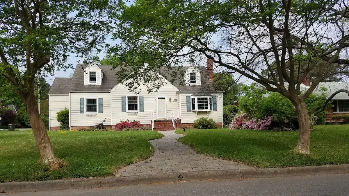 White home with dormers and a curved front walkway framed by trees and flowers